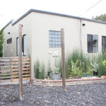 A house with plants and wooden fence in front of it.