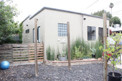 A house with plants and wooden fence in front of it.