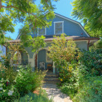 A blue house with many trees and bushes around it