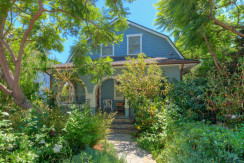 A blue house with many trees and bushes around it