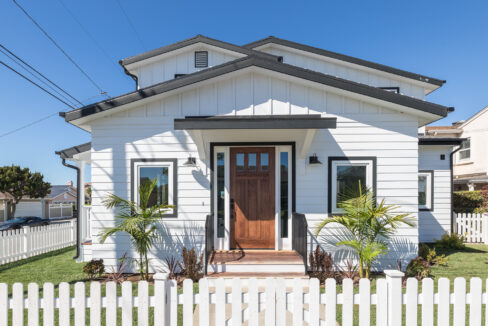 A white house with a picket fence and palm trees.